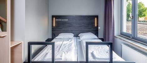 A modern hotel room with a large window, a bed with white linens, and a wooden headboard.