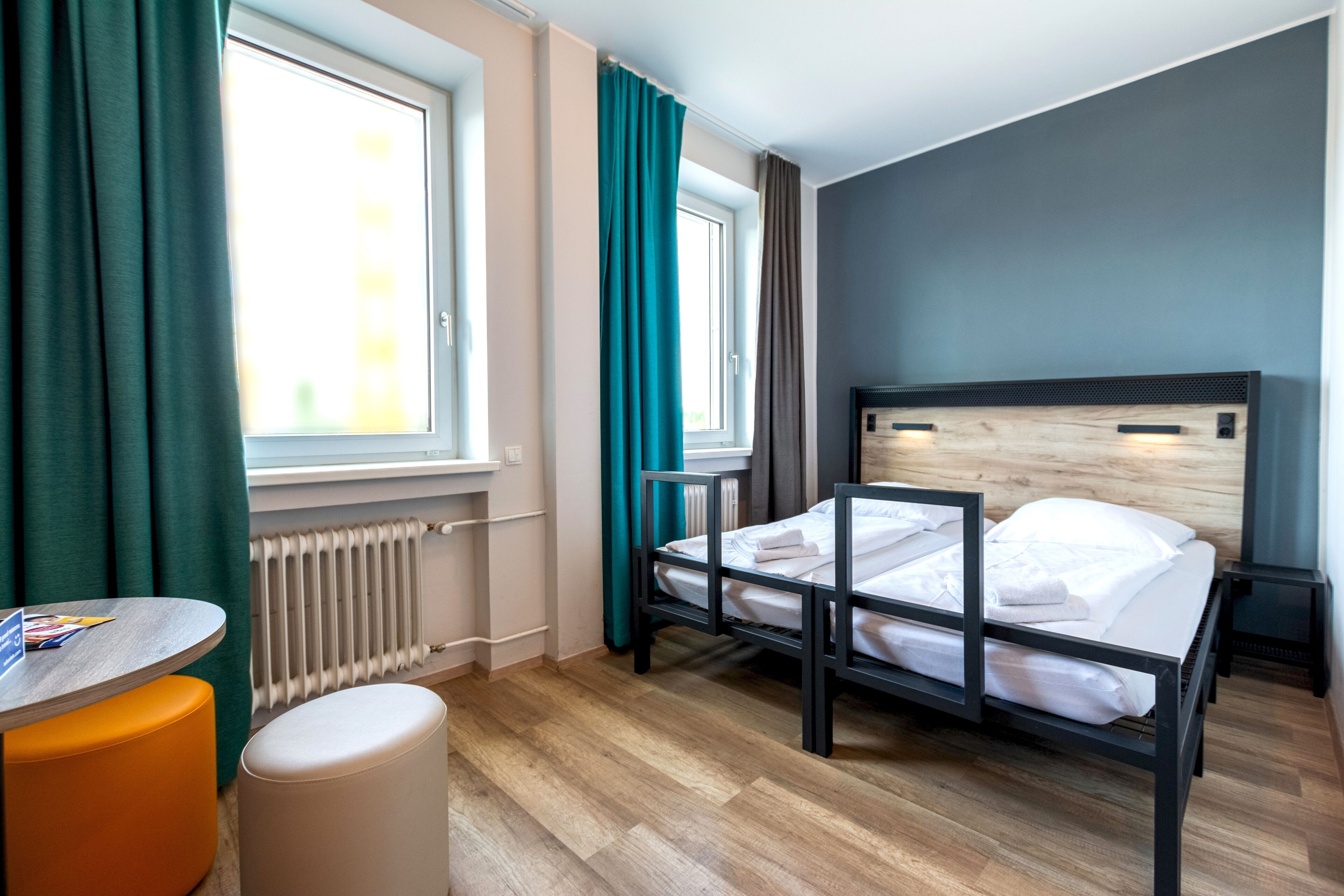 A hotel room with a bed, a small table, and a window with curtains.