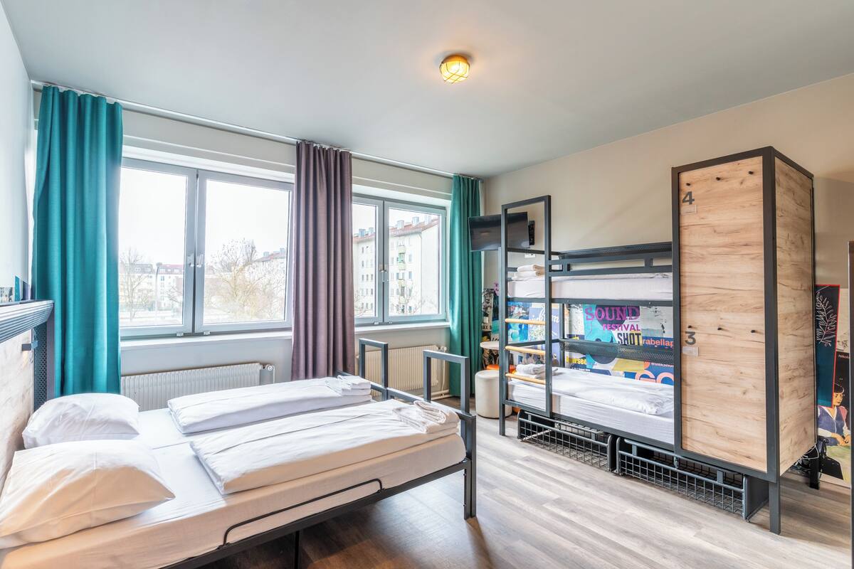 Une chambre de dortoir avec des lits superposés, une fenêtre avec des rideaux, un radiateur et une étagère avec quelques objets.