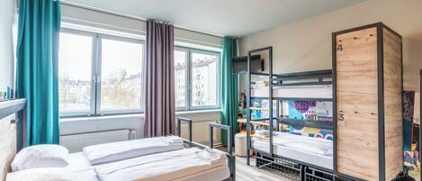 Un dormitorio con literas, una ventana con cortinas, un radiador y una estantería con objetos.