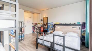 A hotel room with a bed, a desk, a mirror, and a wall with posters.