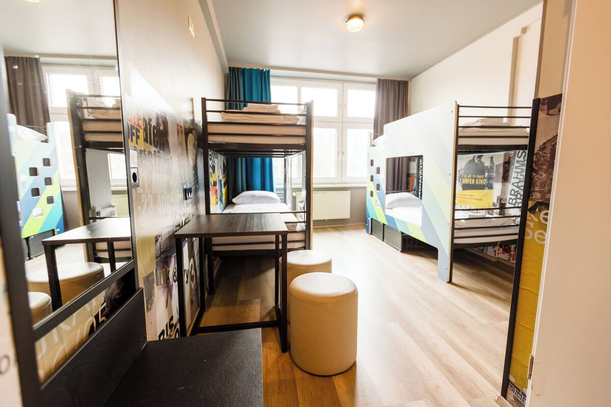 Une chambre de dortoir avec des lits superposés, un bureau et un pouf rond.