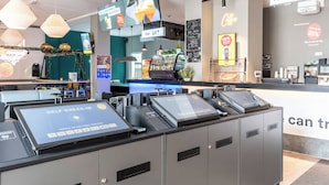 Itsepalveluun tarkoitettu sisäänkirjautumisautomaatti, vastaanottoalue ja baari, joissa on näkyvillä mainoskylttejä.