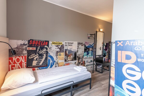 A hotel room with a single bed, a chair, and a wall decorated with various posters.