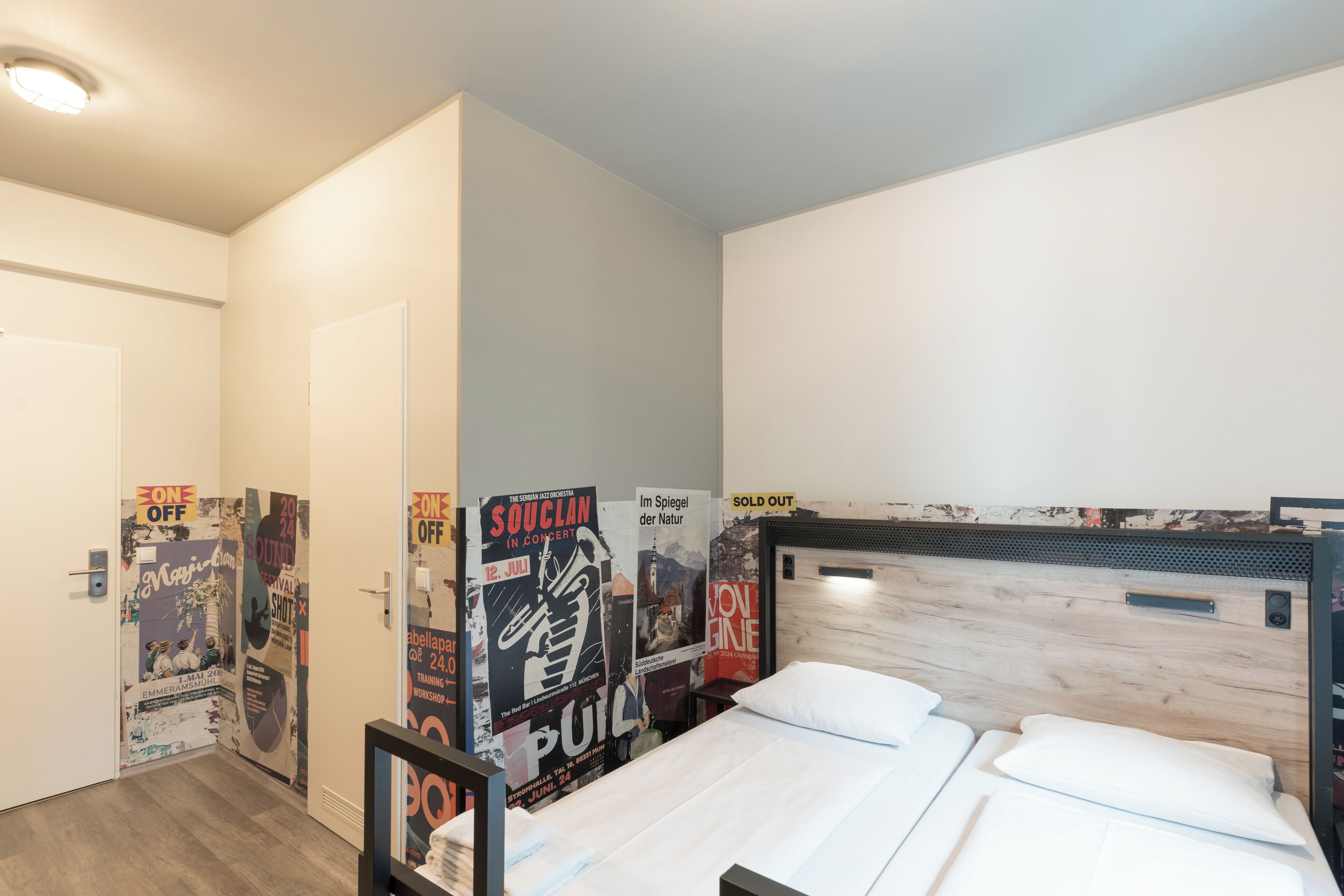 A hotel room with a bed, a wooden headboard, and posters on the wall.