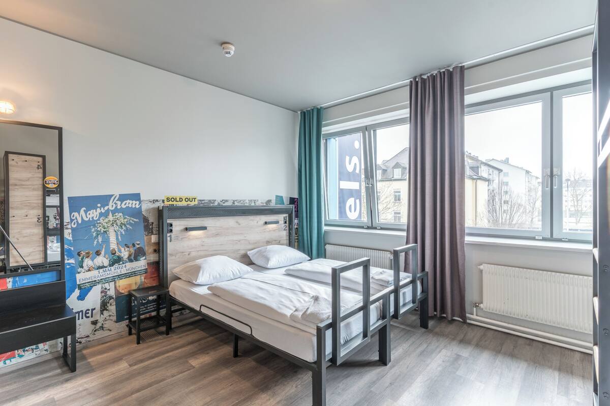 Une chambre moderne avec un plancher en bois, un cadre de lit en métal, une fenêtre avec des rideaux et une affiche accrochée au mur.
