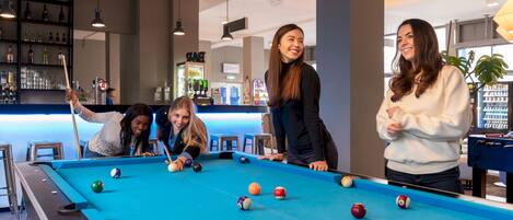 A pool table in a modern indoor setting with a bar area in the background.