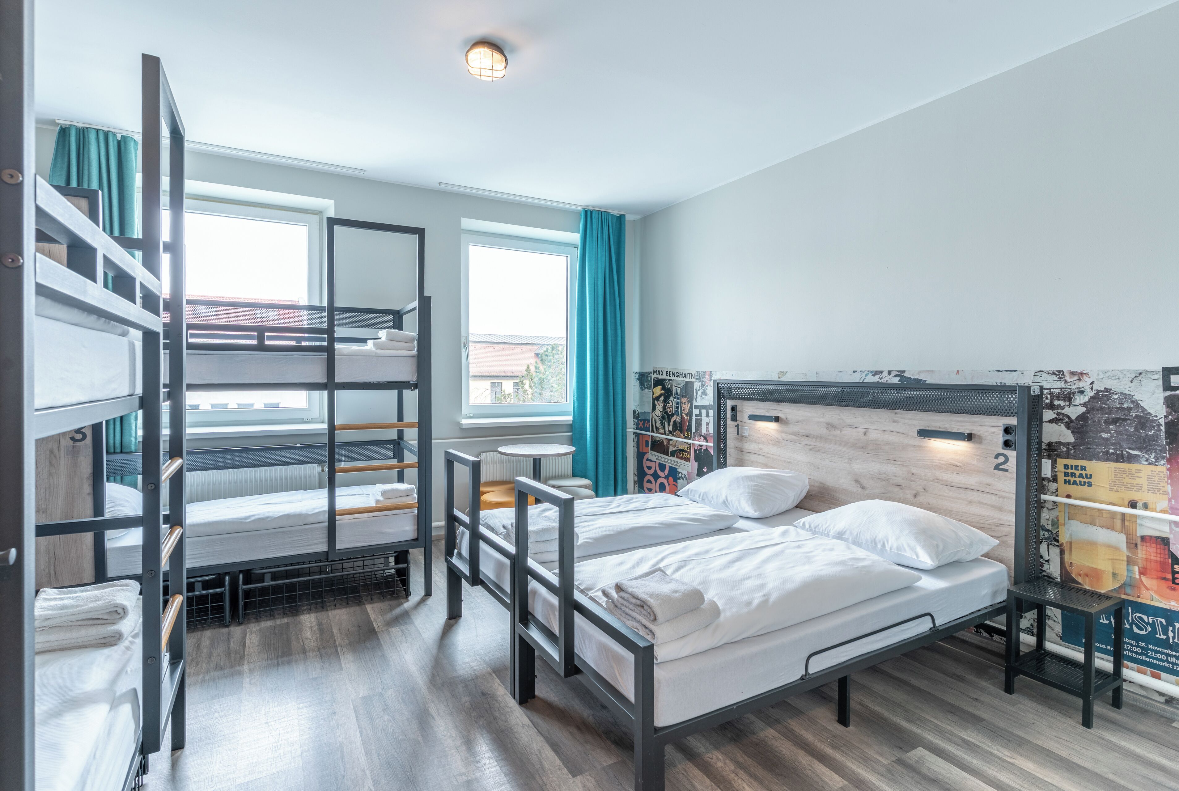 Quarto em dormitório com beliches, uma janela com cortinas, um radiador e um cartaz na parede.