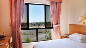 Una habitación con cama, ventana con cortinas, mesita de noche y lámpara.