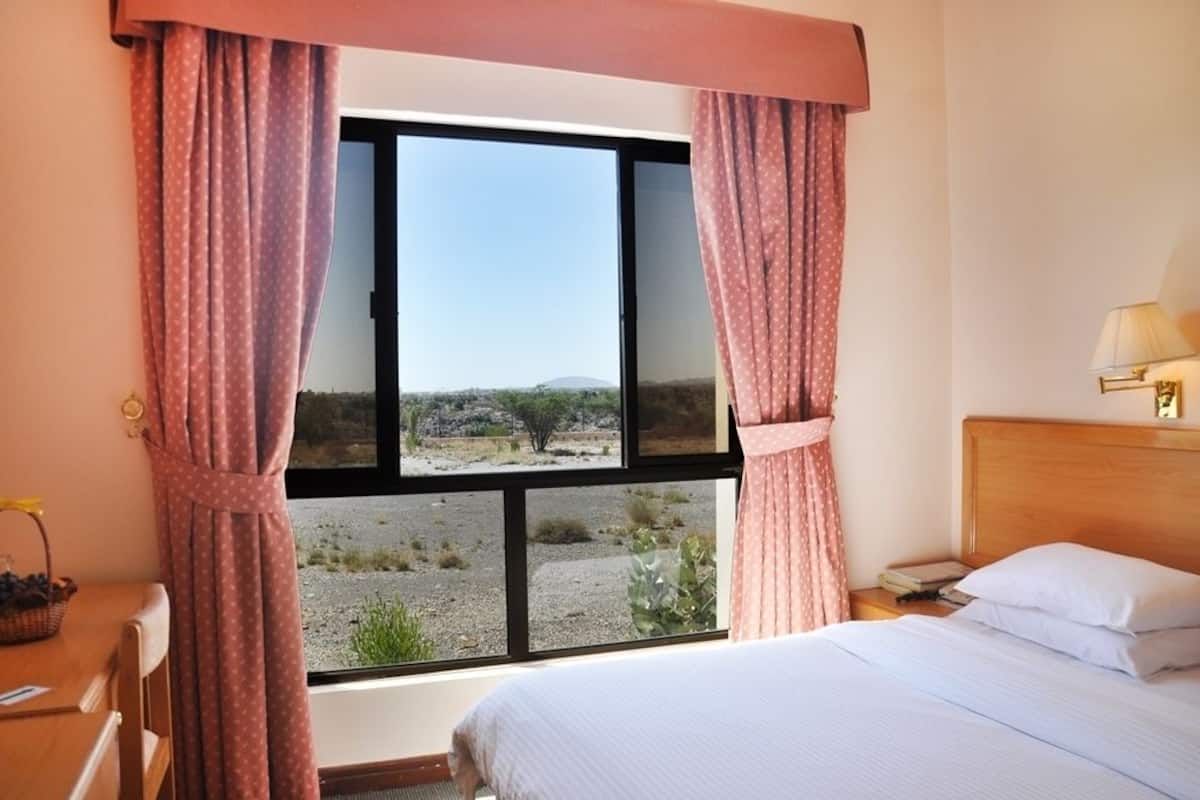 A room with a bed, a window with curtains, a nightstand, and a lamp.
