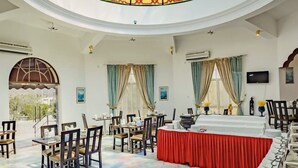 Un comedor amplio con techo alto y una ventana de vitrales. Las mesas están dispuestas con manteles blancos y sillas.