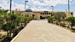 Entrada de hotel con un sendero pavimentado, ventanas arqueadas y un letrero que indica un restaurante.