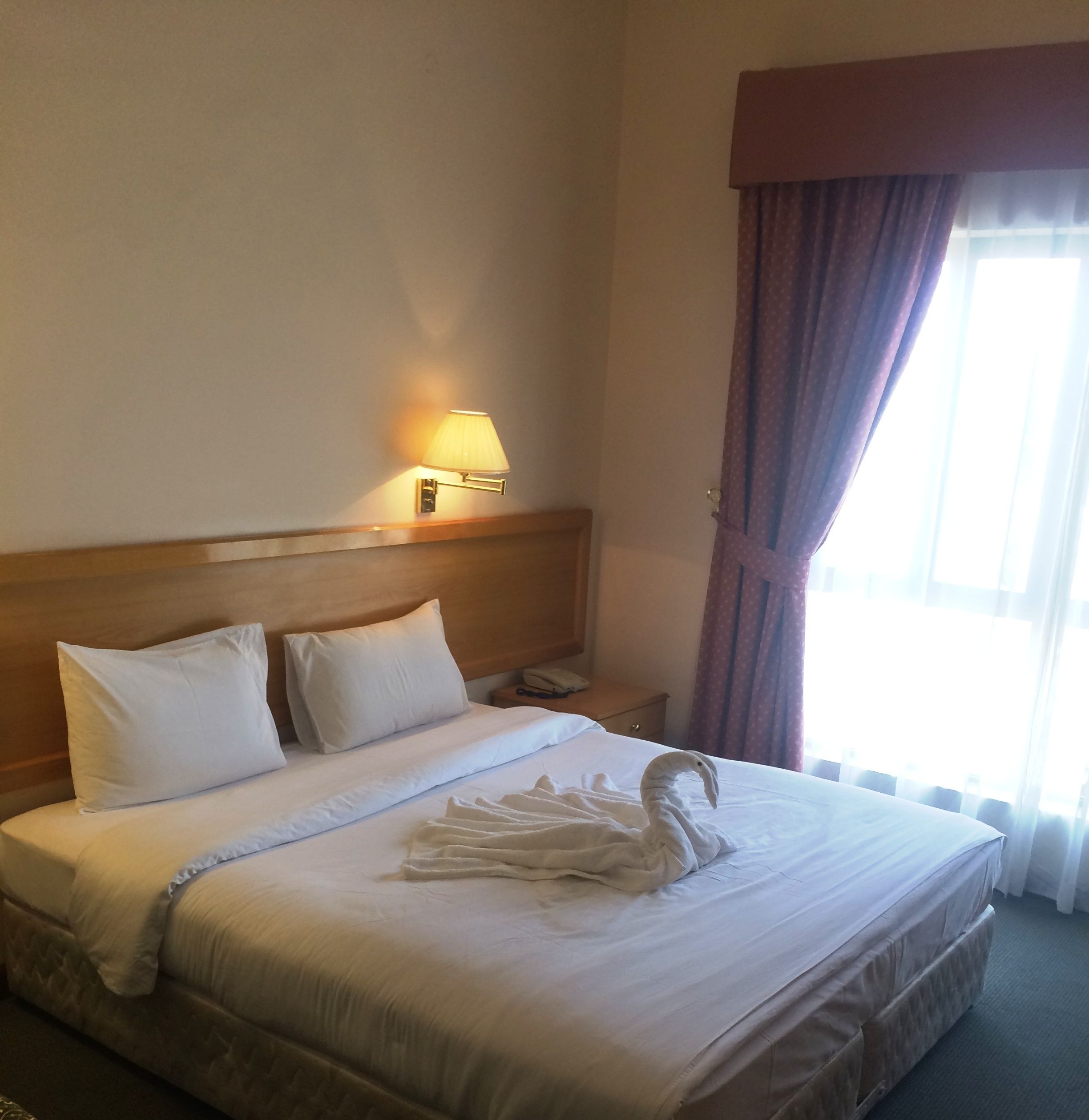 A hotel room with a neatly made bed, a bedside lamp, a telephone, and a window with curtains.