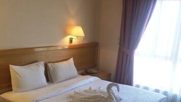 A hotel room with a neatly made bed, a bedside lamp, a telephone, and a window with curtains.
