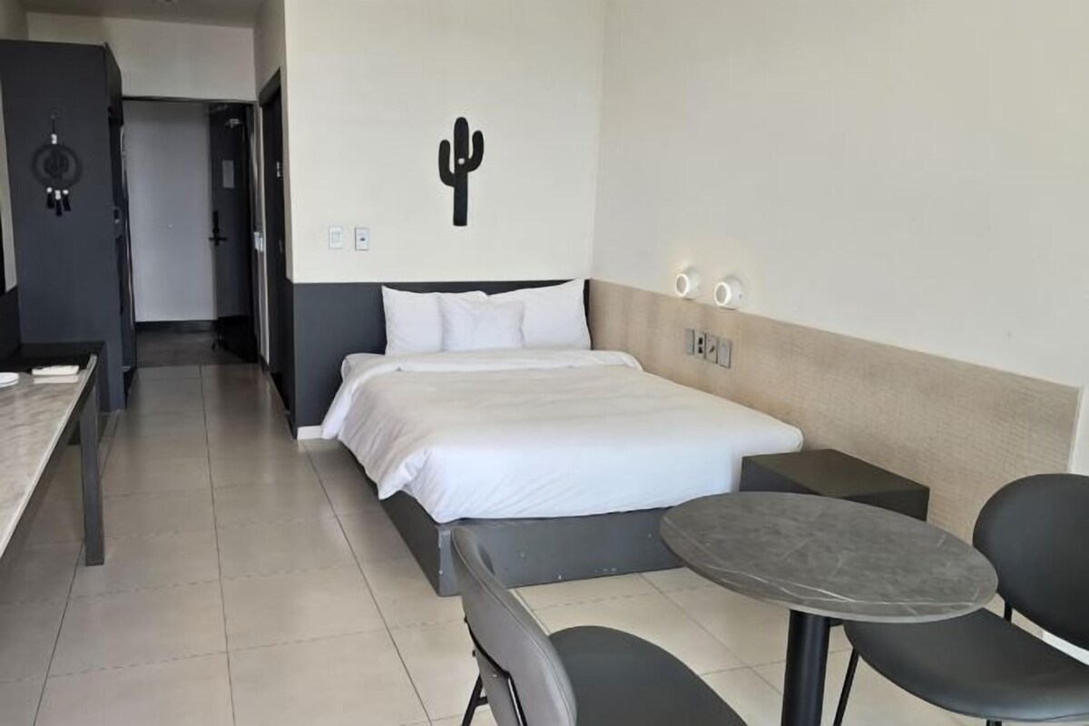 Ein Hotelzimmer mit Bett, Schreibtisch, Stuhl, einem kleinen Tisch und einer Wanddekoration mit einem Kaktus.