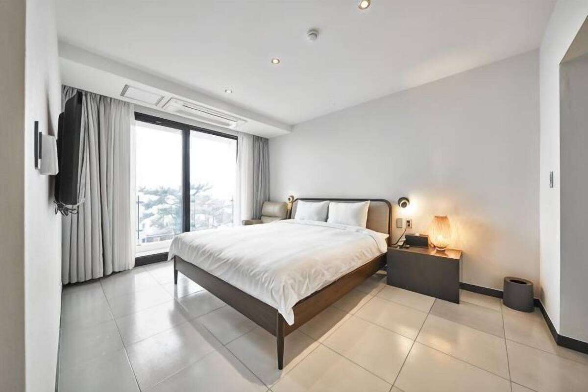 Une chambre d’hôtel moderne avec un grand lit, une table de chevet avec une lampe, une télévision et une vue sur la ville.