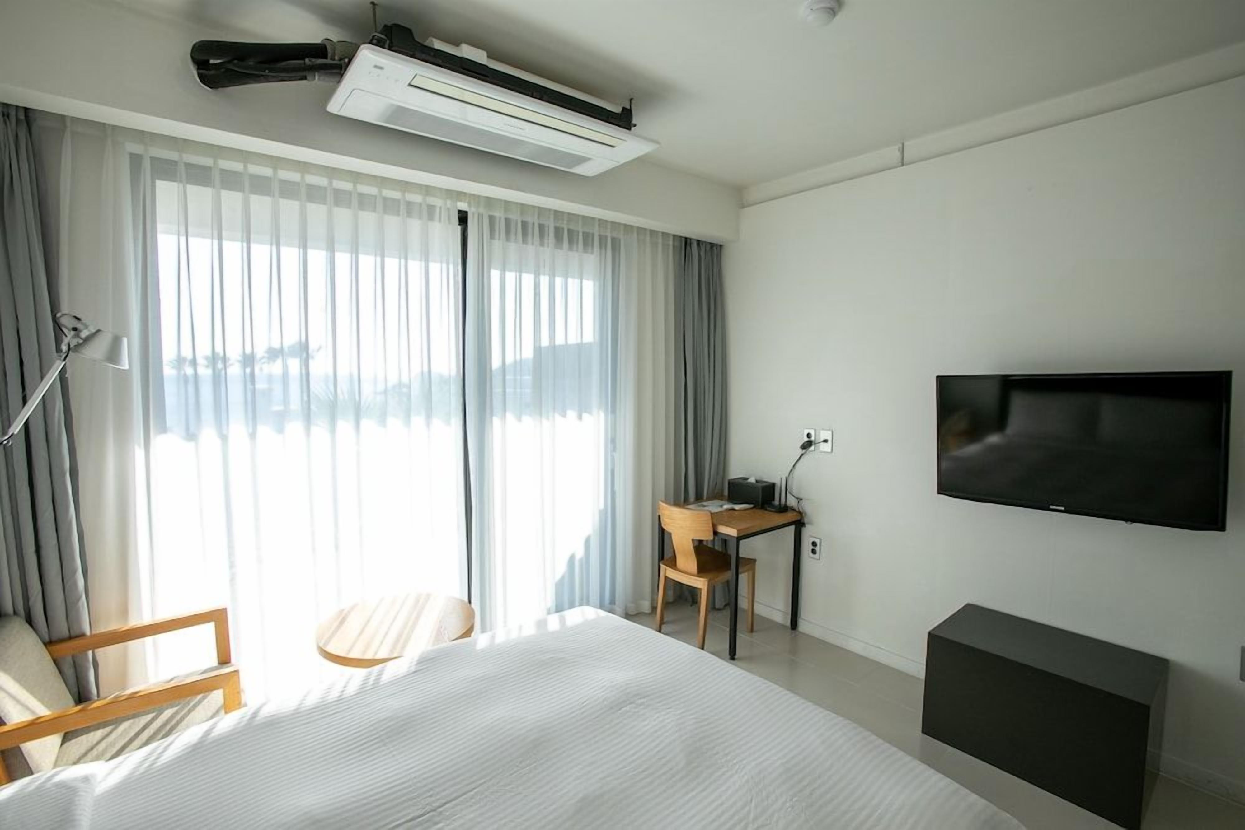 Habitación de hotel con cama, escritorio, silla, televisor y aire acondicionado.