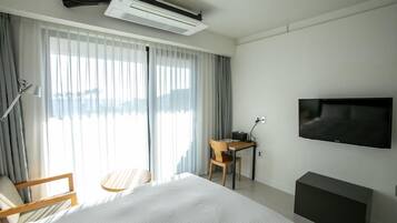 Habitación de hotel con cama, escritorio, silla, televisor y aire acondicionado.