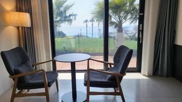 A room with two chairs and a table, large windows with a view of palm trees and the sea.