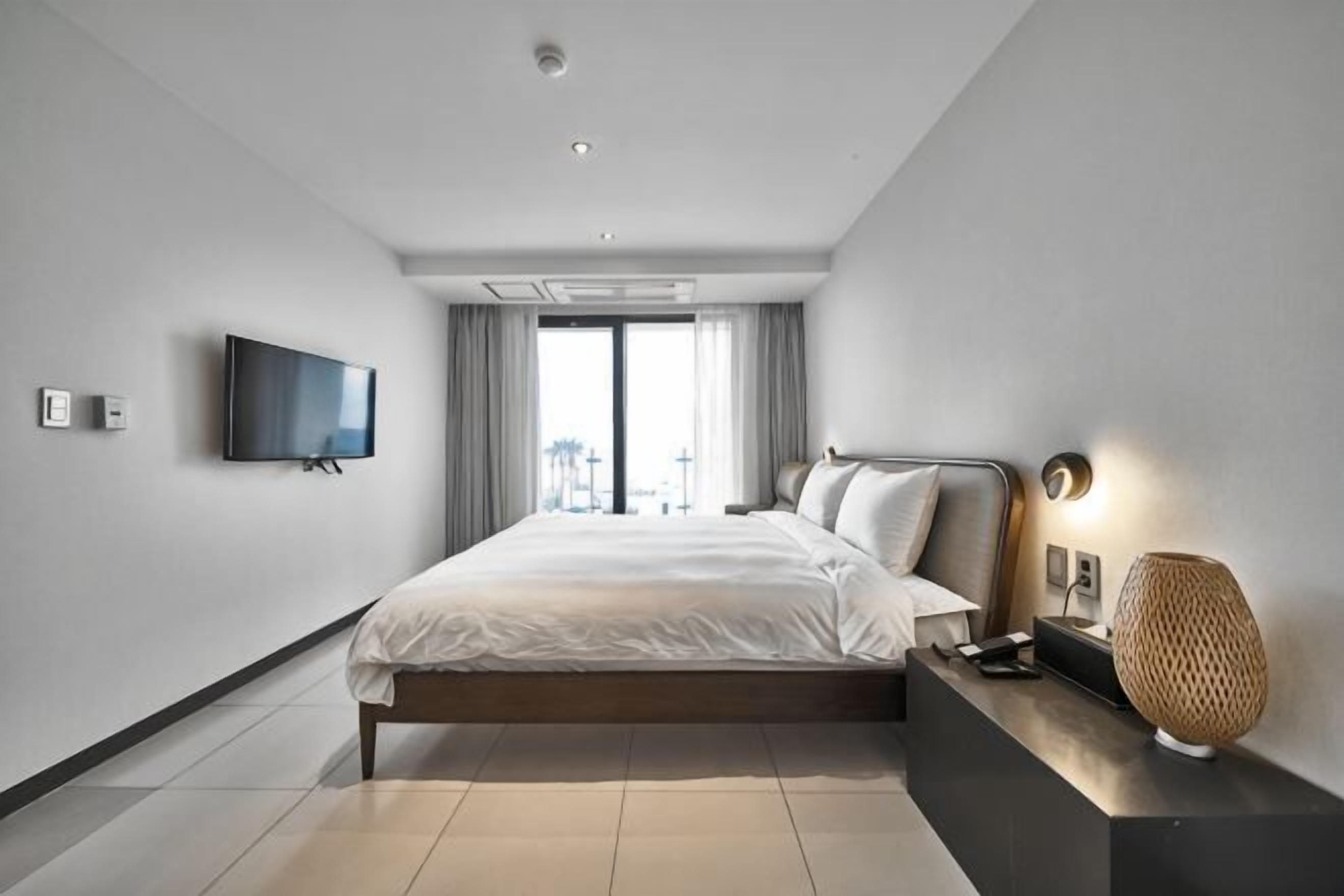 Une chambre d’hôtel moderne dotée d’un grand lit, d’une télévision à écran plat, d’une table de chevet avec une lampe et offrant une vue sur la ville.