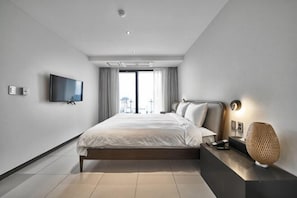 Une chambre d’hôtel moderne dotée d’un grand lit, d’une télévision à écran plat, d’une table de chevet avec une lampe et offrant une vue sur la ville.