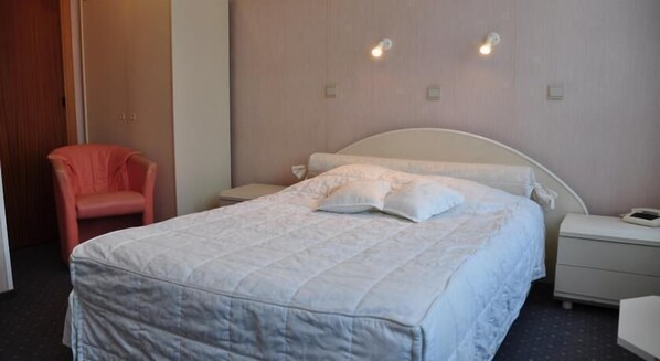 Una habitación de hotel con una cama, una silla y una mesita de noche con teléfono.