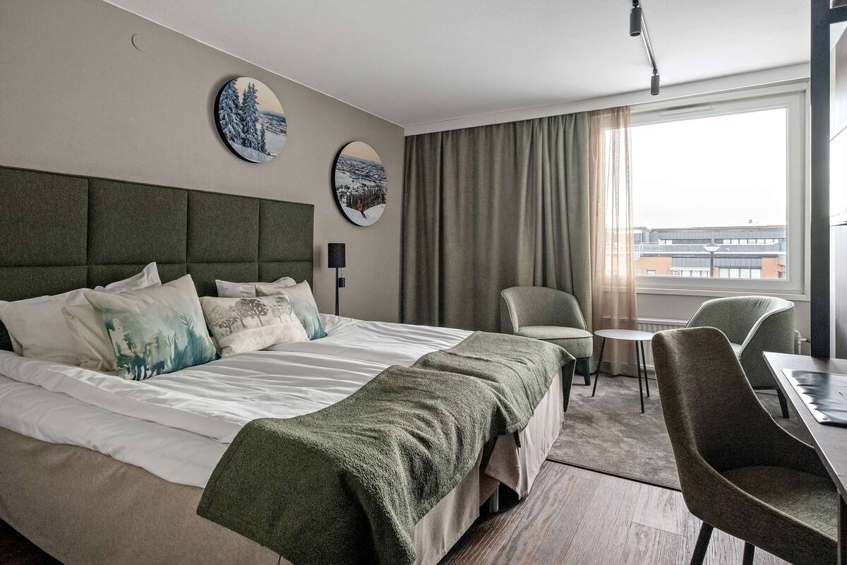 Ein Hotelzimmer mit einem großen Bett, einem Esstisch, zwei Stühlen, einem kleinen Tisch, einer Lampe und zwei runden Spiegeln an der Wand.