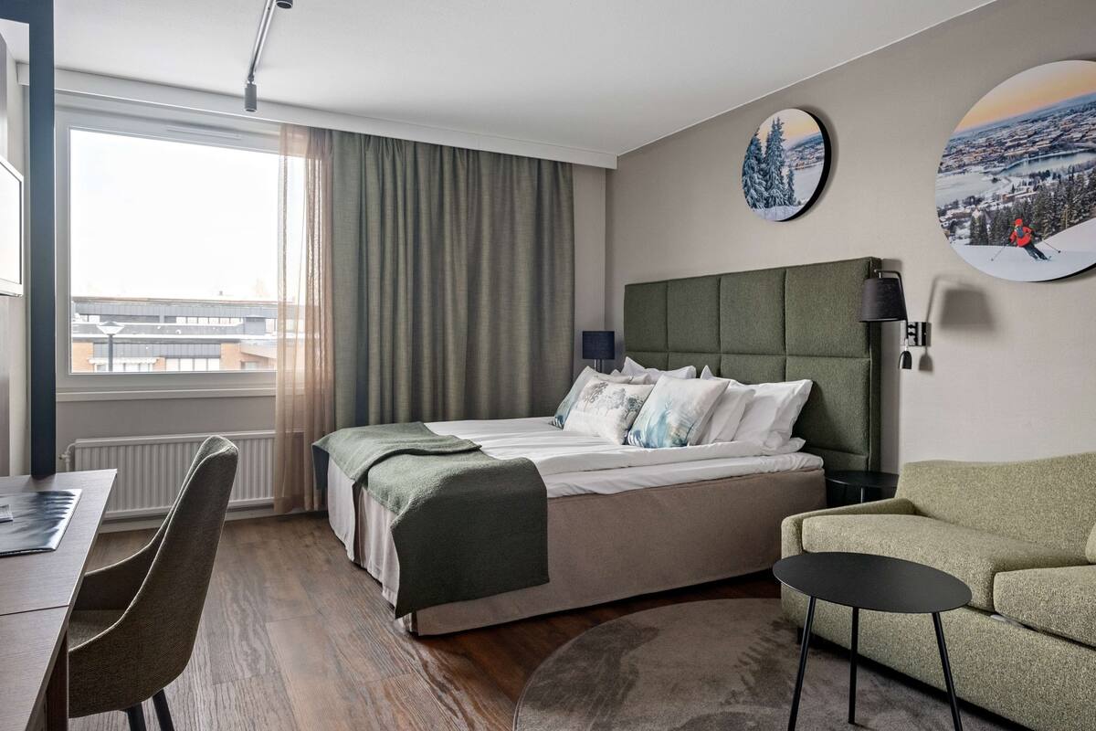 Ein modernes Hotelzimmer mit einem großen Bett, einem Schreibtisch, einem Sessel, einer Couch und zwei Wandleuchten.
