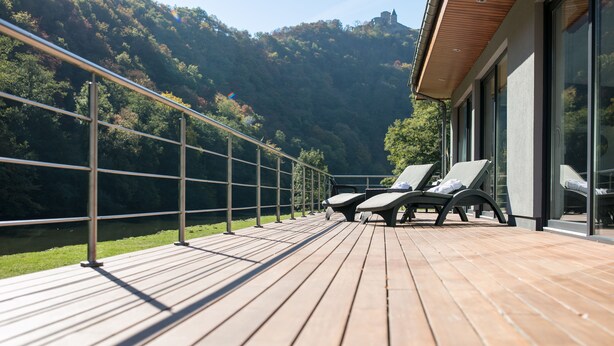 Una terraza de madera con sillones de descanso con vista a un lago y colinas boscosas.
