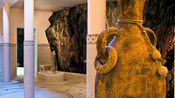 Un grand vase d’aspect rustique, doté d’une anse en corde, un mur en pierre et un sol carrelé dans le hall d’un hôtel.