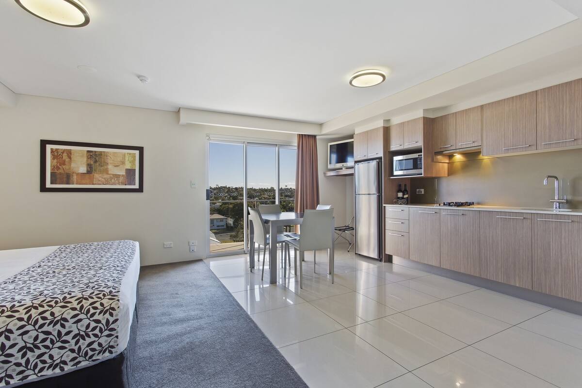 A modern hotel room with a balcony, a dining area, and a kitchenette.