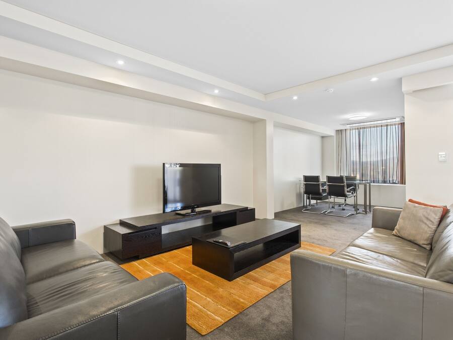 A modern living room with a flat-screen TV, leather sofas, and a wooden coffee table.