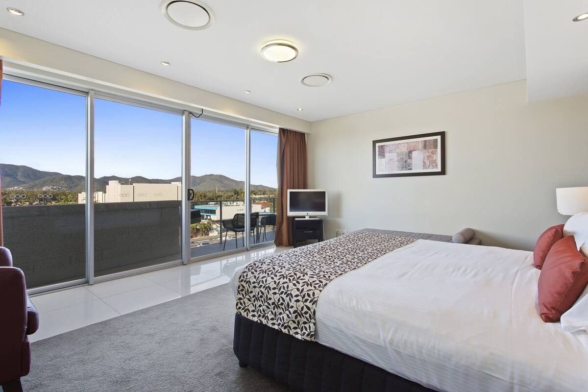A modern hotel room with a large bed, a television, and a balcony with a city view.