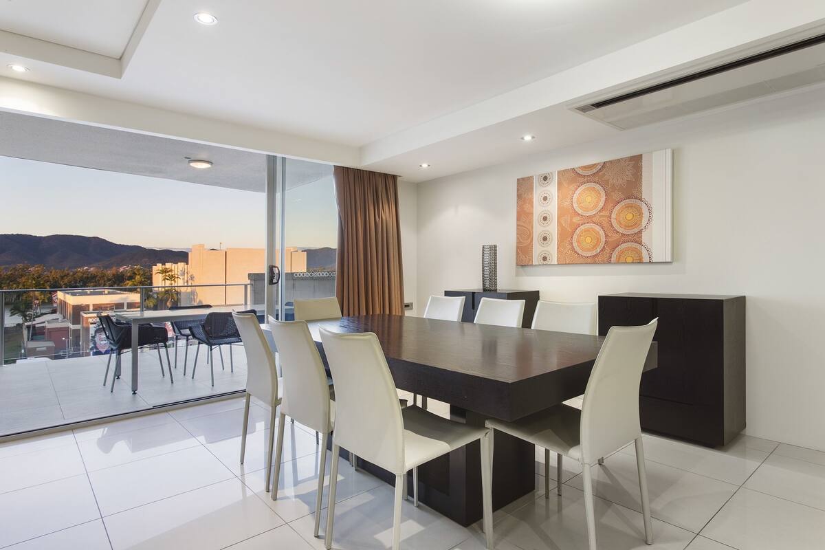 A modern dining area with a large table and chairs, a glass partition, and a city view.