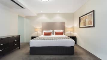 Ein modernes Schlafzimmer mit einem großen Bett, Nachttischlampen, einer dunklen Kommode und einem gerahmten Kunstwerk an der Wand.