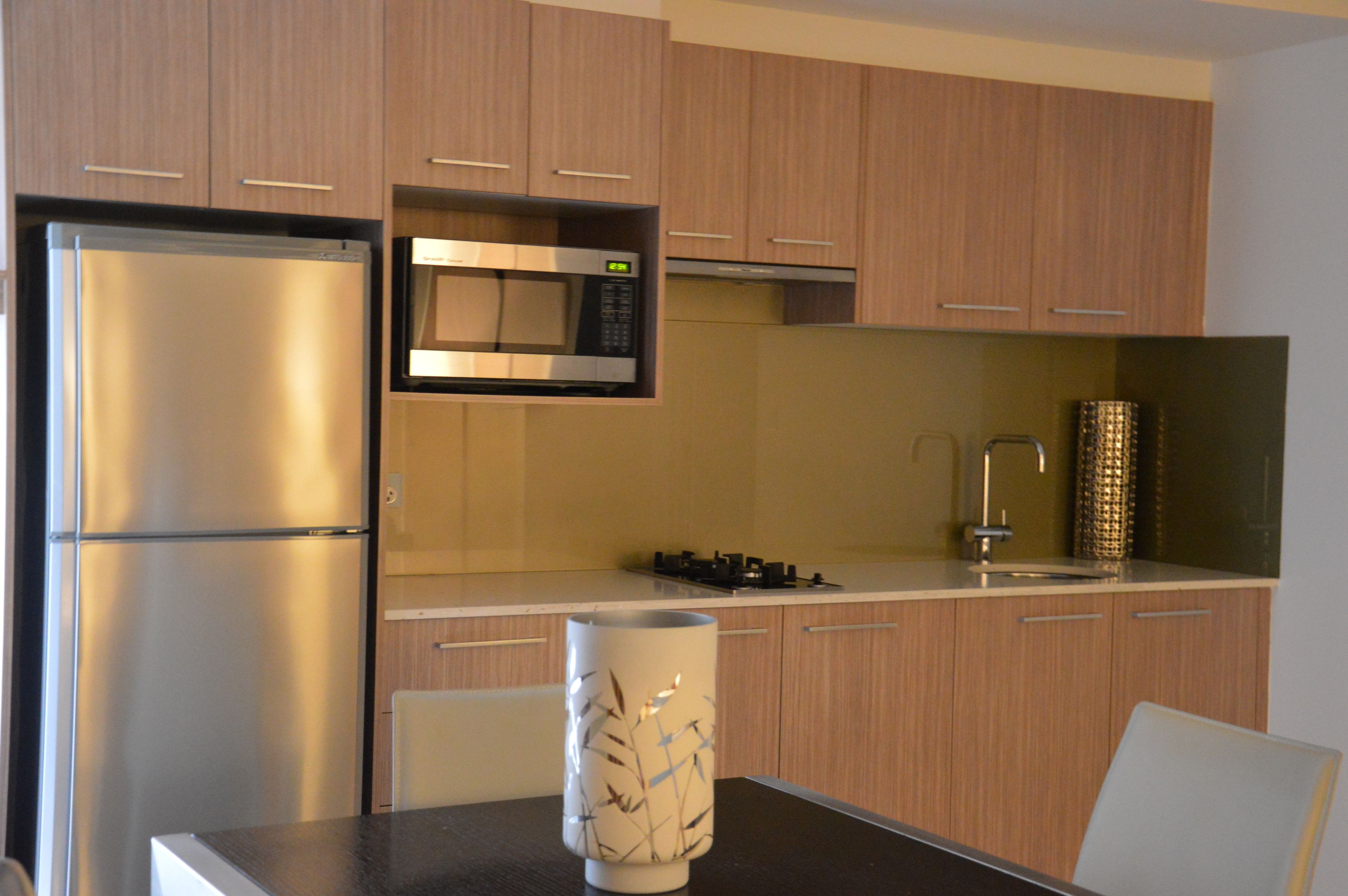 A modern kitchen with wooden cabinets, a stainless steel refrigerator, a microwave, and a gas stove.