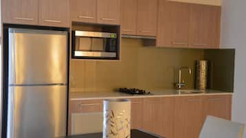 A modern kitchen with wooden cabinets, a stainless steel refrigerator, a microwave, and a gas stove.