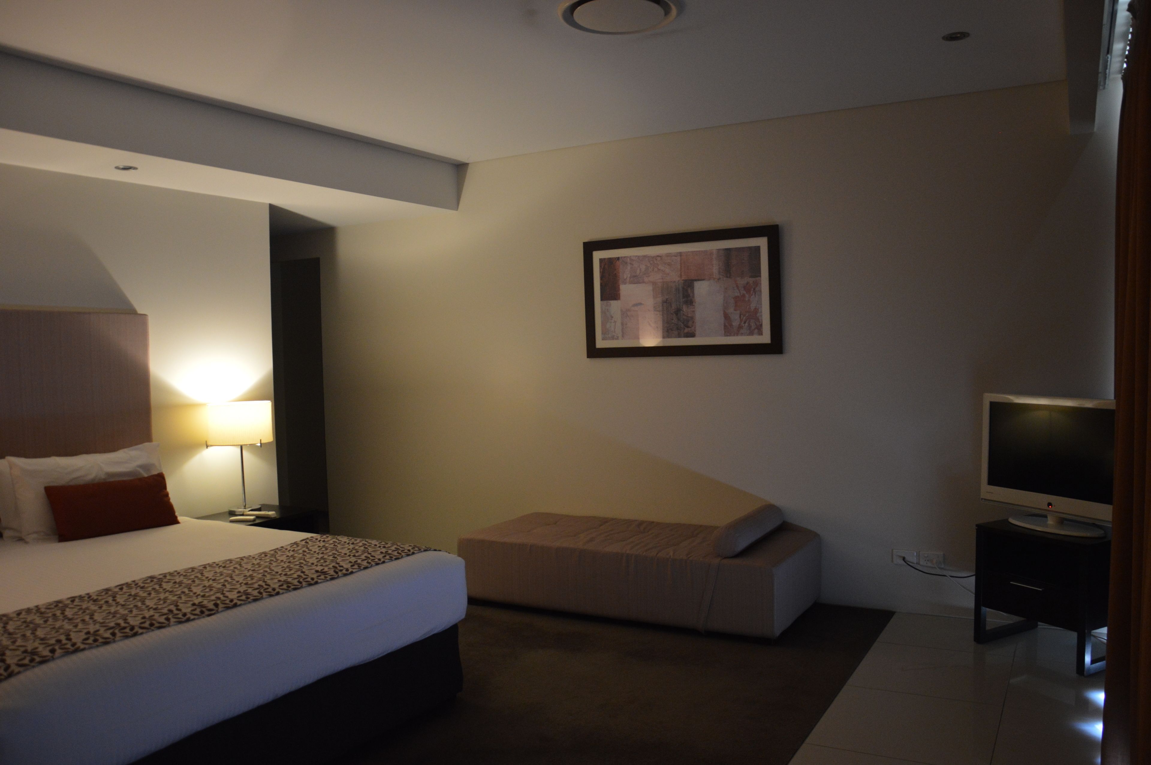 Una habitación de hotel moderna con una cama grande, un sofá pequeño, un televisor de pantalla plana y una obra de arte enmarcada en la pared.