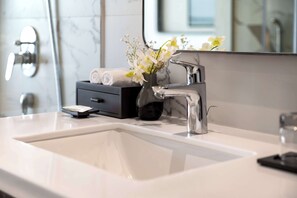 Une salle de bain moderne avec un lavabo blanc, un robinet chromé et un vase contenant des fleurs blanches.