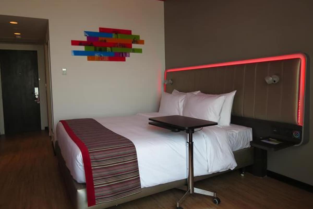 Ein modernes Hotelzimmer mit Bett, Nachttisch, Wandbild und einer roten Akzentwand.