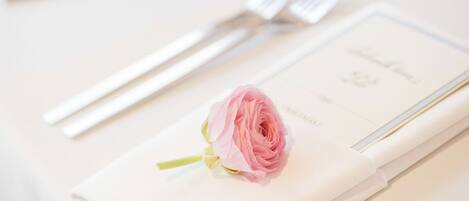 A neatly arranged table setting with a folded napkin, a pink rose, and silver cutlery.