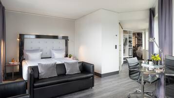 Una habitación de hotel moderna con una cama grande, un sofá, un escritorio con una silla y una pequeña mesa con lámpara.