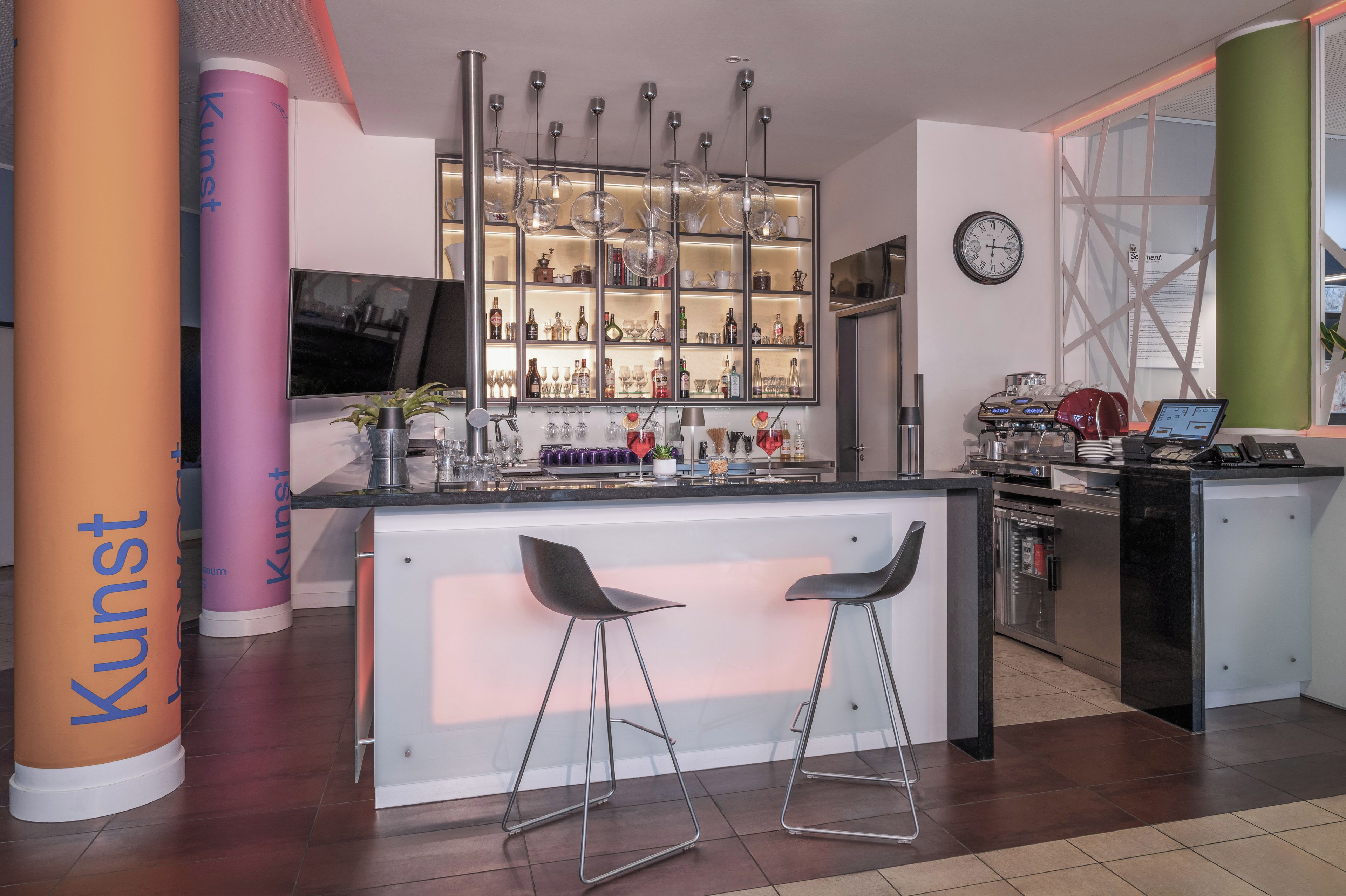 A modern kitchen with a bar area, including a refrigerator, oven, and coffee machine.