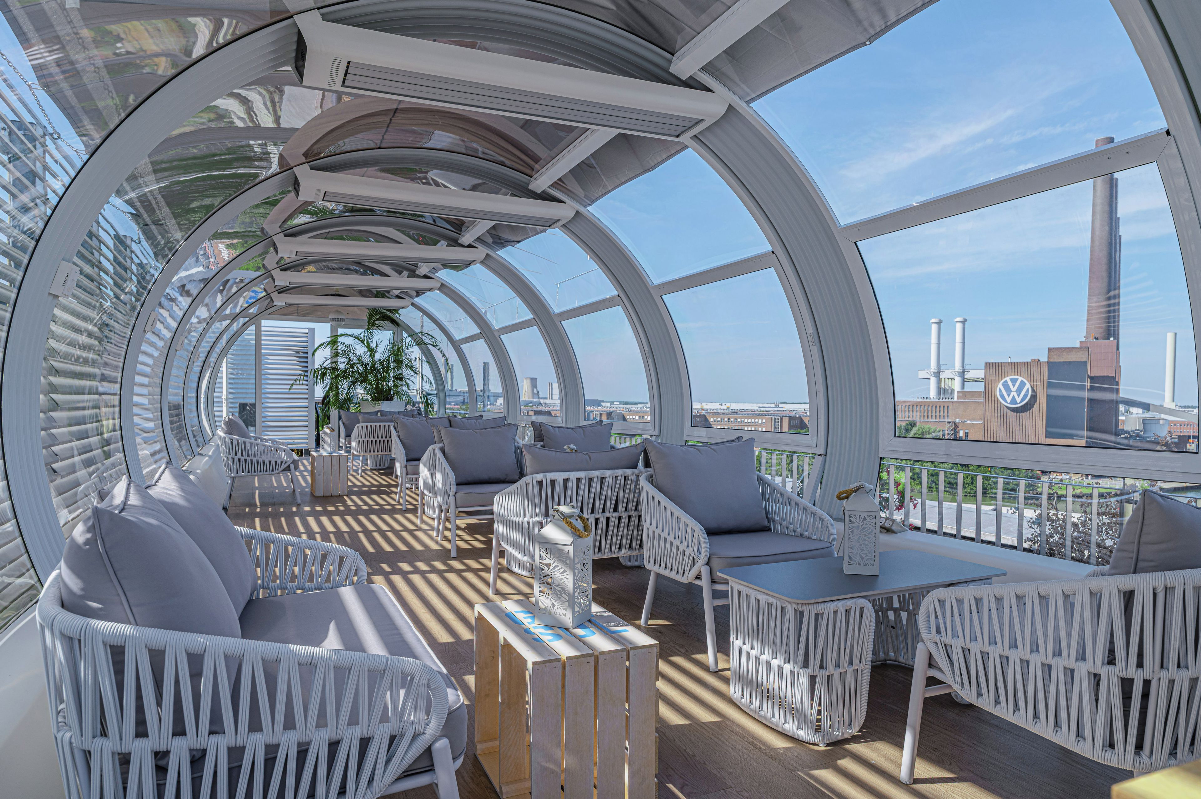 Eine moderne, geschwungene Dachterrasse mit weißen Rattanmöbeln und freiem Blick auf die Stadtlandschaft.