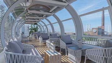 Eine moderne, geschwungene Dachterrasse mit weißen Rattanmöbeln und freiem Blick auf die Stadtlandschaft.