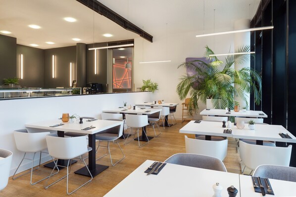 Ein modernes Restaurant mit weißen Tischen und Stühlen, einer Bar und Topfpflanzen.