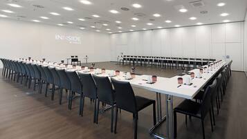 A conference room with long tables, chairs, and a projection screen displaying "INSIDE BY MELIA".