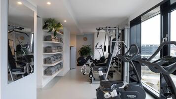 A modern gym with exercise equipment, a large mirror, and a view of the city through large windows.