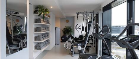 Un gimnasio moderno con equipamiento de ejercicio, un espejo grande y vistas de la ciudad a través de amplias ventanas.
