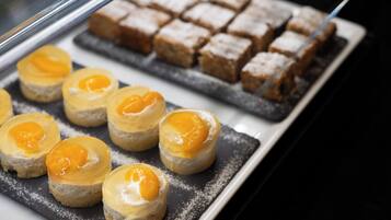 A display case with desserts, including small pastries with a yellow topping and a tray of square desserts dusted with powdered sugar.